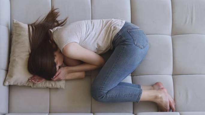 悲伤沮丧的女人独自躺在胎儿位置的沙发上
