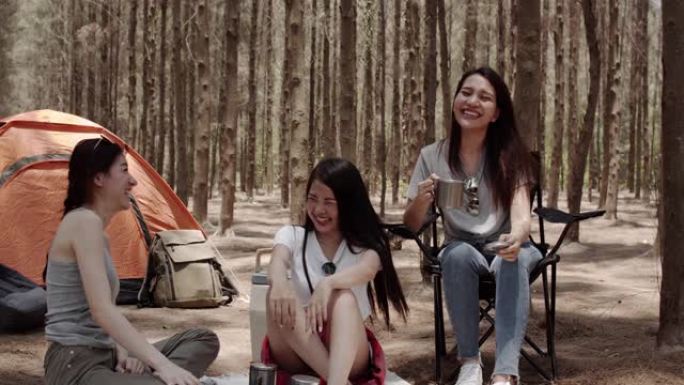 一群年轻的亚洲朋友在森林里露营或野餐，十几岁的女性喜欢在帐篷前聊天。妇女在夏季进行冒险活动并在假期度