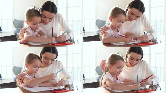 有爱心的妈妈拥抱帮助小女儿用铅笔画画