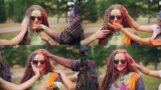 快乐朋友的慢动作用粉末涂料画漂亮女孩的脸和头发在Holi节上，女人戴着墨镜笑着笑。