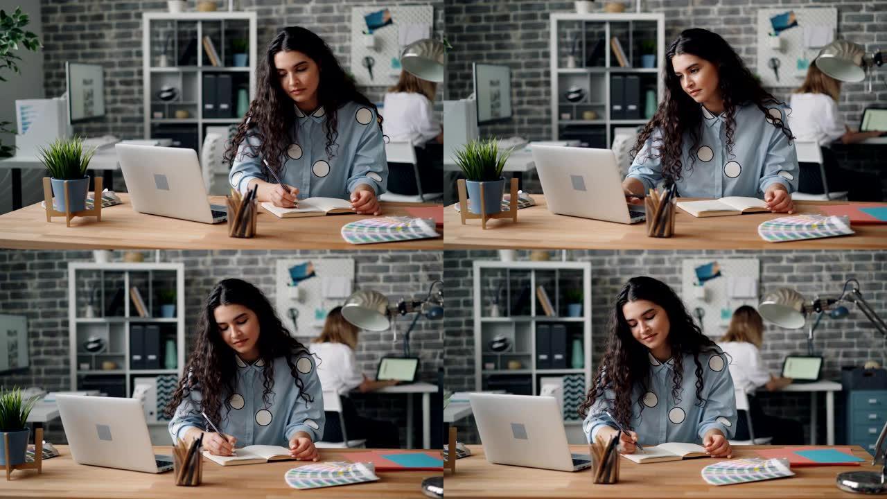 漂亮的年轻女士在笔记本上写字，在办公室用笔记本电脑工作