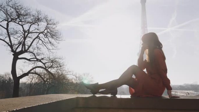 美丽快乐的白人女人穿着红色连衣裙坐着，在史诗般的日出巴黎埃菲尔铁塔天空风景慢动作。