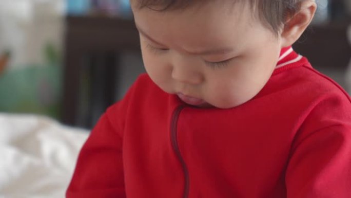 穿着红色连衣裙的亚洲8个月女婴喜欢在家白色床上玩耍。