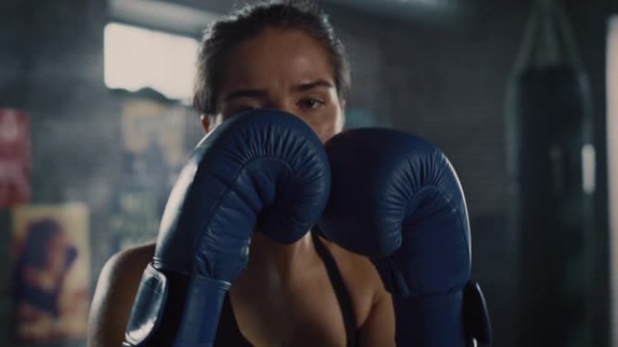 一位美丽健康的黑发跆拳道运动员在镜头前摆姿势，双手戴着蓝色战斗手套。女孩在镜头前挥拳。她在地下健身房