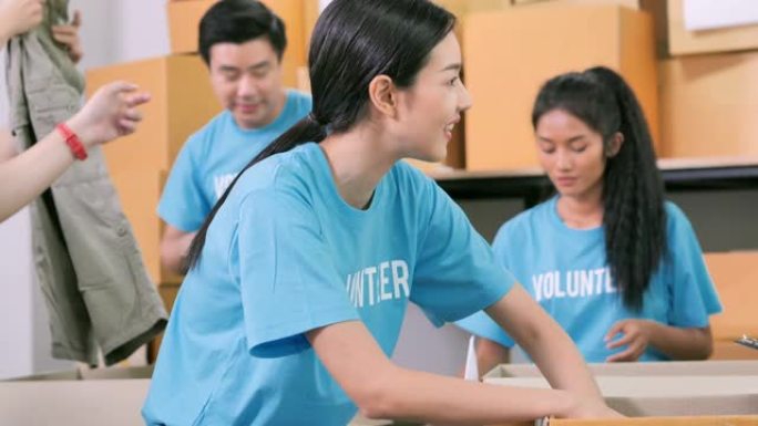 亚洲年轻女子快乐与朋友志愿者打包衣服捐赠给无家可归的人。友谊，团队，成功，志愿，领导，人，慈善理念。