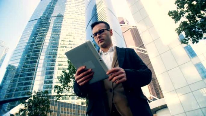 人在摩天大楼背景上使用平板电脑，仰视图。