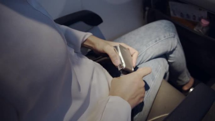 坐在飞机上，穿着白衬衫的亚洲女性乘客系好安全带。