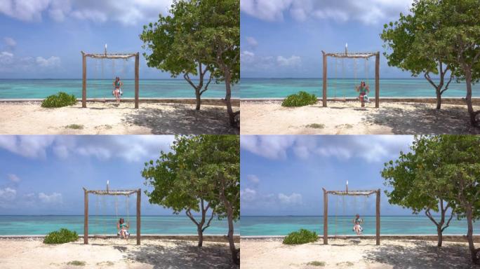 快乐的女孩在马尔代夫白色沙滩上的浪漫秋千上摇摆。