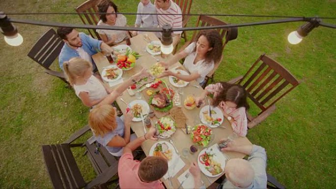 大家庭游园会庆典，聚集在餐桌上的亲朋好友，年轻人和老人都在吃喝玩乐。自上而下的相机拍摄。