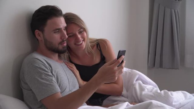 年轻夫妇坐在床上用手机视频通话