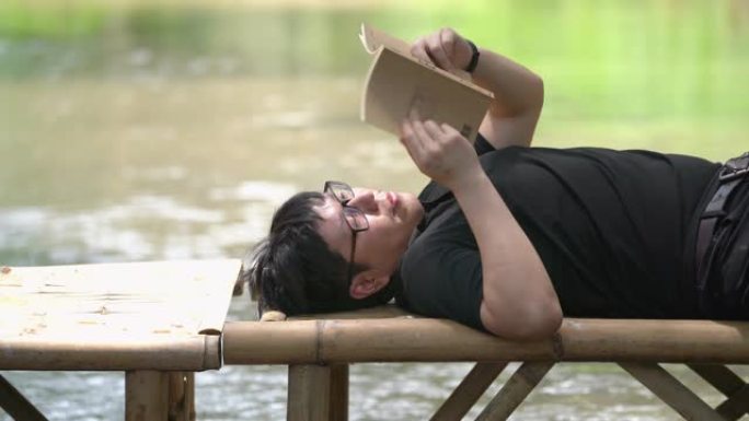 亚洲男子放松躺在木桥上看书