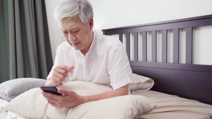高清慢动作: 亚洲成熟成年人使用智能手机，坐在床上。安慰、关心和开朗的理念。