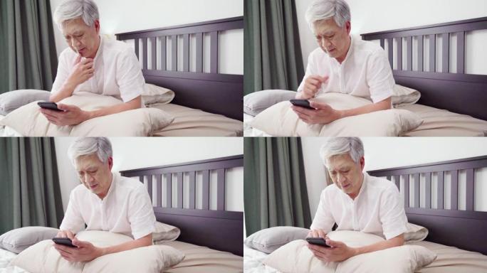 高清慢动作: 亚洲成熟成年人使用智能手机，坐在床上。安慰、关心和开朗的理念。