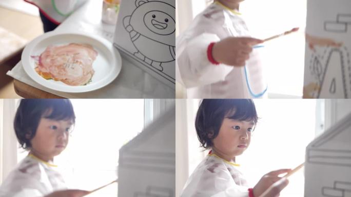 亚洲儿童在家建造和绘画玩具纸板屋。