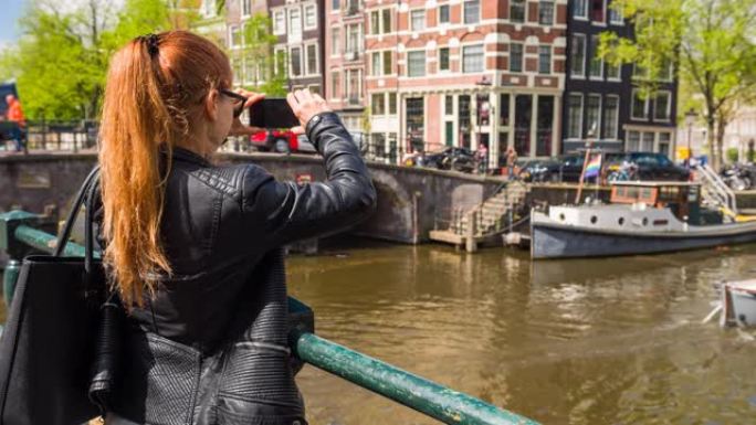 开朗的女人拍摄荷兰阿姆斯特丹的运河，对着镜头微笑