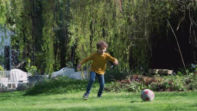 小男孩在家里的花园里踢足球
