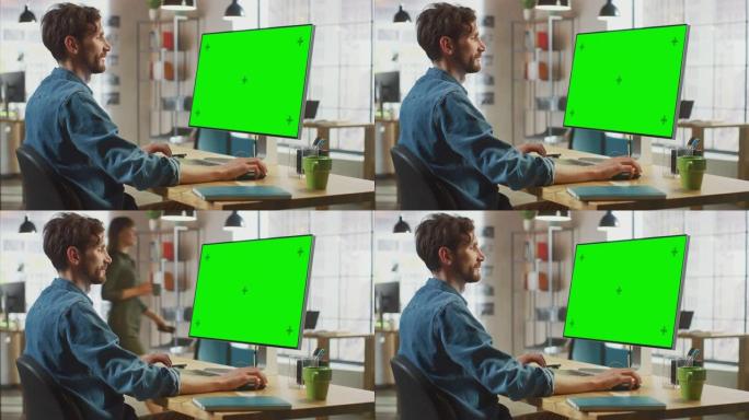留着胡须和牛仔裤衬衫的男性创意设计师在他的个人计算机上工作，并带有绿色大屏幕模拟显示。他在一个很酷的