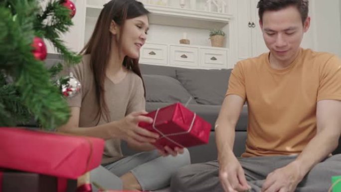 亚洲夫妇包装和包装圣诞礼物在圣诞节期间装饰他们家里的客厅。生活方式男女快乐庆祝夏季圣诞节和新年概念。