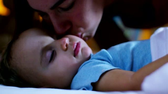 漂亮的妈妈在睡觉前给她的宝宝一个前吻，用羊毛材料上的粉色和蓝色毯子非常甜蜜地覆盖她，温暖