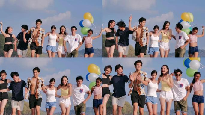 一群朋友带着气球在蓝天的背景下在海滩上散步。幸福的朋友在夏天阳光明媚的阳光下在海滩上玩耍。假期-iS