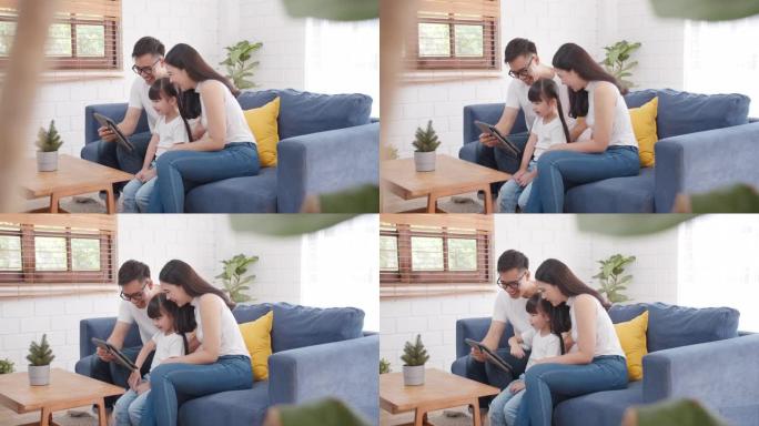 慢动作宽镜头: 幸福温暖的家庭父亲，母亲和女儿一起坐在沙发上的数字平板电脑上在线观看有趣的电视，父母