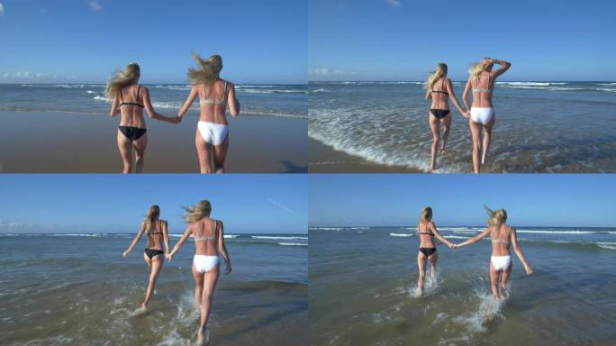 南非海滩上两个美丽的年轻女子在海浪中奔跑的4k后视图
