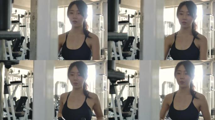 迷人的女人在健身房的跨界机器上锻炼。在健身中心用举重训练机训练年轻的运动型亚洲女性。慢动作。锻炼和运