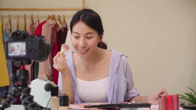 慢动作-美容博主介绍美容化妆品坐在前置摄像头中录制视频。快乐美丽的年轻亚洲女人使用化妆品评论化妆教程