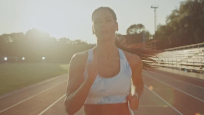 浅蓝色运动上衣的美丽健身女子在户外体育场慢跑。她在一个温暖的夏日下午跑步。运动员在赛道上进行体育练习
