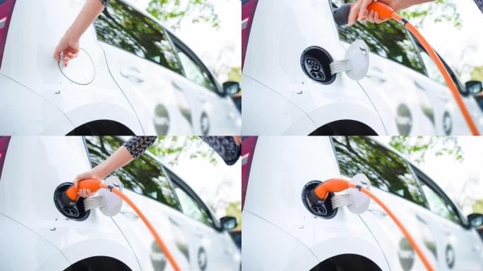 女人在电动插电式车辆上将电动汽车插入充电站首选在郊区停车