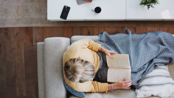 头顶镜头低头看着躺在读书和喝咖啡的女人