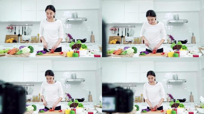 年轻的亚洲女性影响者vlogger穿着白色西装，在厨房里看着镜头。相机缩小