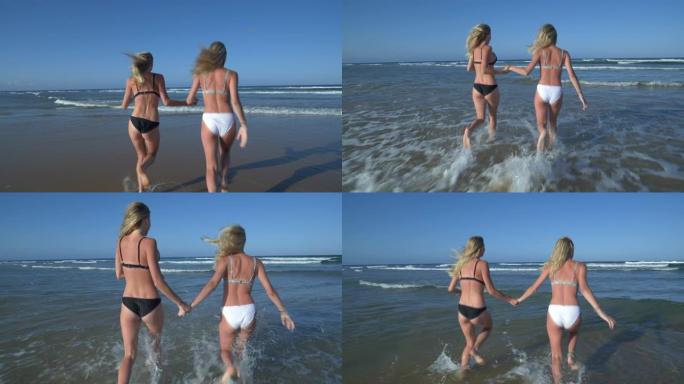 南非两个漂亮的年轻金发女人跑进海里的4k特写后视图
