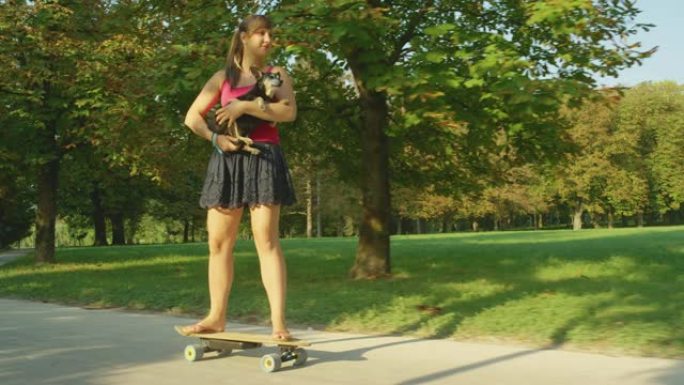 慢动作: 快乐的女人在骑电子滑板时抱着她的高级狗。