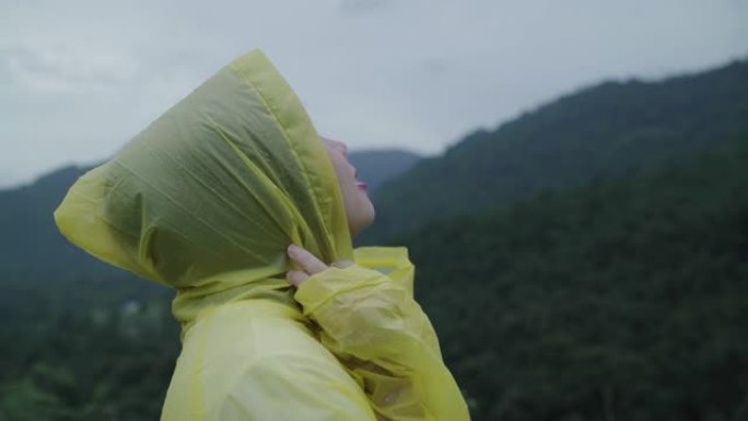 年轻的亚洲妇女穿着雨衣在森林附近散步时感到很开心。生活方式女性在雨天享受和放松。