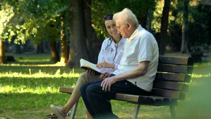 一个保姆，一个护士，照顾老人一个女孩 (女人) 和祖父坐在平装本上看书，在公园里。