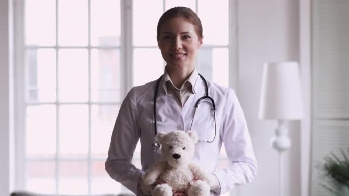 快乐女医生儿科医生抱着泰迪熊看相机
