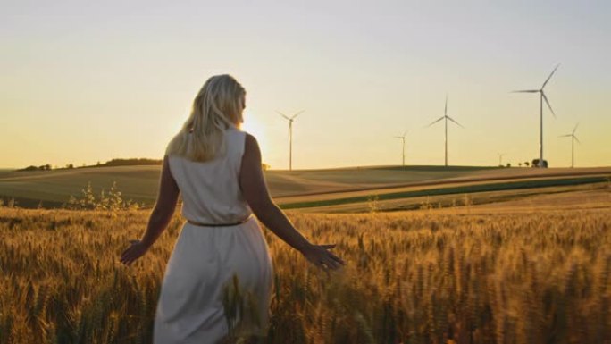 一名妇女一边抚摸着小麦，一边在田里散步，远处有风力涡轮机