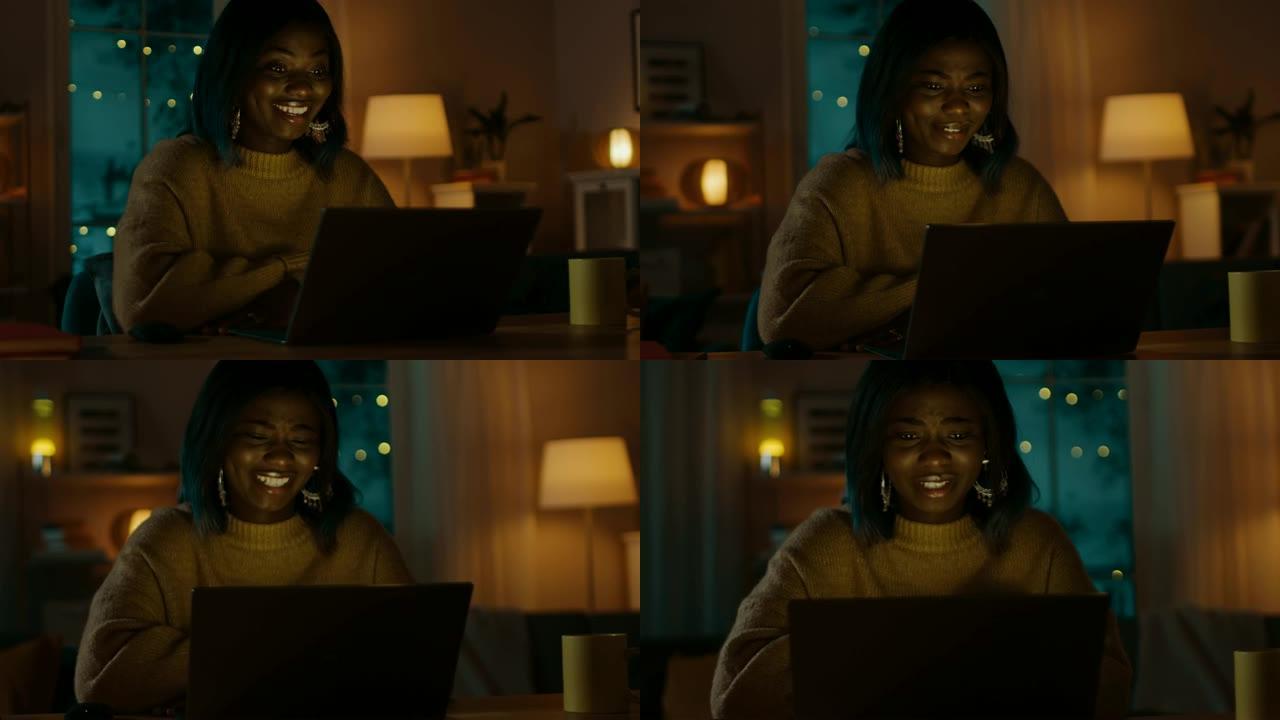 美丽微笑的黑人女孩的肖像坐在她的办公桌前，用笔记本电脑打视频电话，打招呼。晚上，女孩使用计算机网络摄