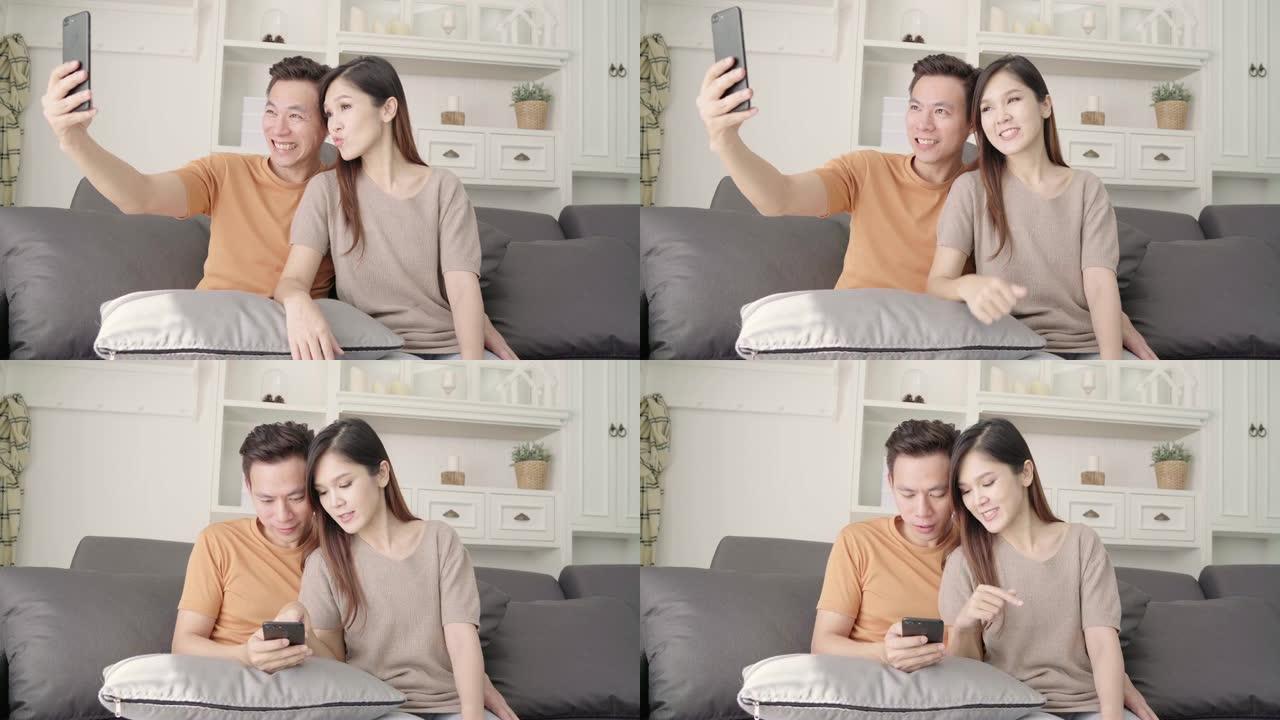 亚洲情侣在家客厅使用智能手机自拍，甜蜜的情侣在家放松时躺在沙发上享受爱情时刻。生活方式夫妇在家放松的
