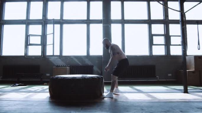 极限锻炼，肌肉发达的年轻赤膊男子在健身房侧视慢动作训练时用巨大的轮胎锻炼。
