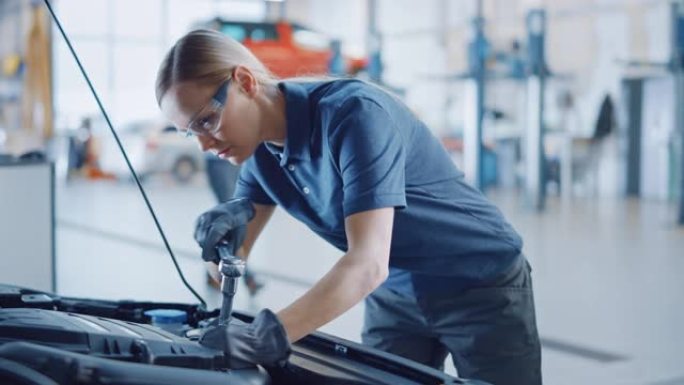 美丽的赋能女机械师正在汽车服务中工作。戴安全眼镜的女人正在修理发动机。她在用棘轮。现代汽车清洁车间。