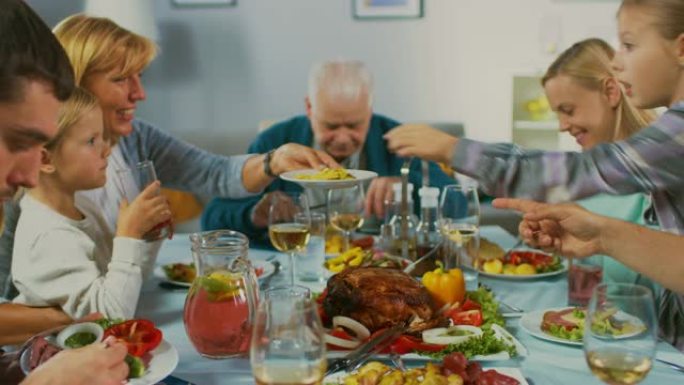 大家庭和朋友在家里庆祝，各种各样的年轻人和老人聚集在餐桌旁。吃饭、分享食物、喝酒和娱乐。白天的节日。