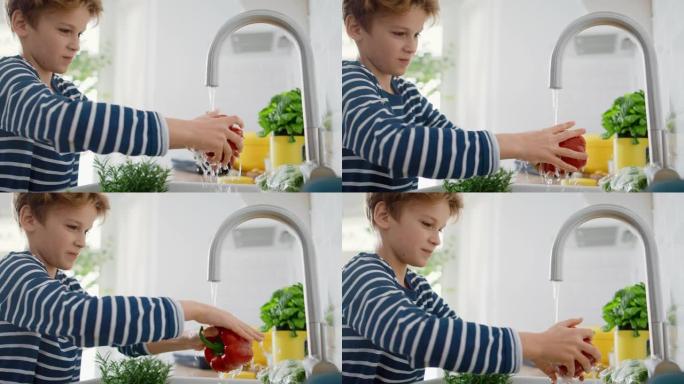在厨房里: 聪明的小男孩准备沙拉，洗甜椒，其他蔬菜，还有他的手在自来水下的水槽里。聪明的小男孩的肖像