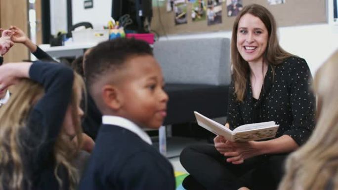女教师给坐在教室地板上的小学生读书，选择性地集中注意力