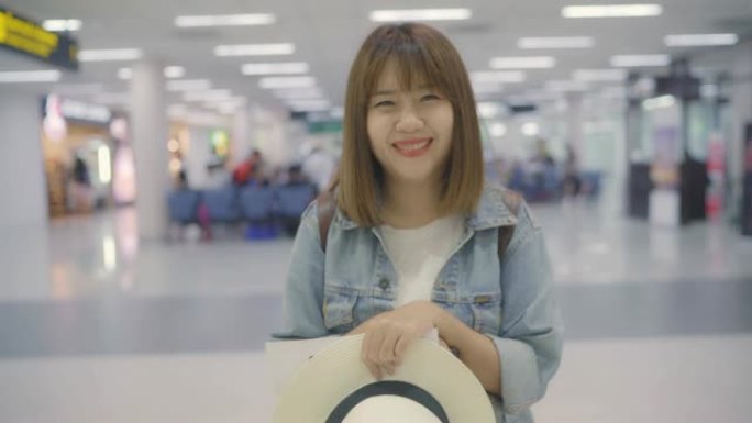 快乐的亚洲女人在国际机场候机楼微笑着对着镜头，女游客准备度假。生活方式女性快乐假期在机场概念。