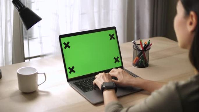 亚洲妇女坐在办公桌前使用带有绿色模拟屏幕的笔记本电脑