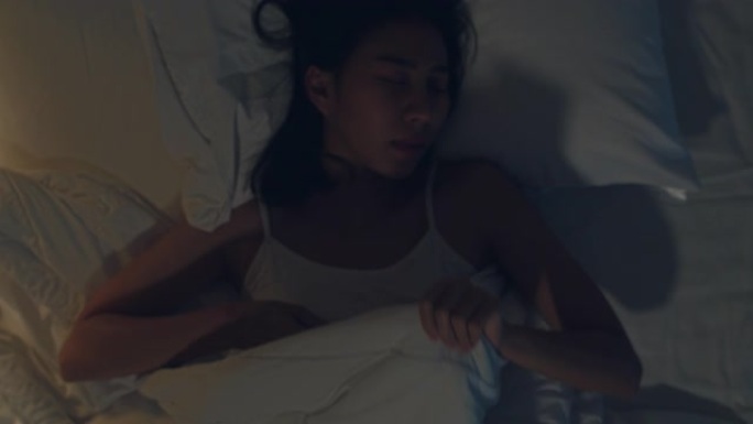 紧张的年轻亚洲女子半夜躺在家里卧室的床上做噩梦。患有头痛或偏头痛，失眠，睡眠呼吸暂停或压力概念。顶视