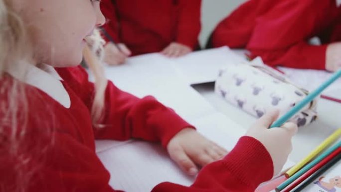 年轻的白人女学生在婴儿学校教室的桌子上画画，特写，过肩视图