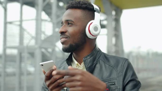 戴着耳机的非裔美国人在户外使用智能手机唱歌